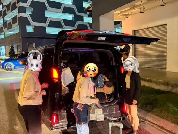 A group loading luggage into a black van at night outside an apartment building