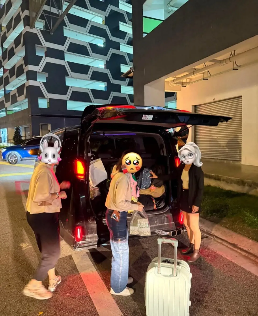 A group loading luggage into a black van at night outside an apartment building