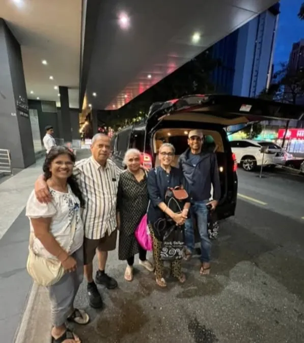 A group posing beside a black van outside a hotel entrance at night
