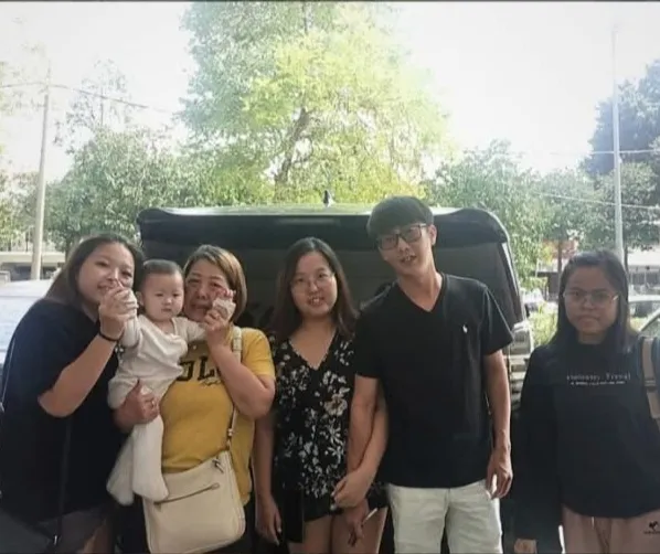 A family with a baby posing beside a black van