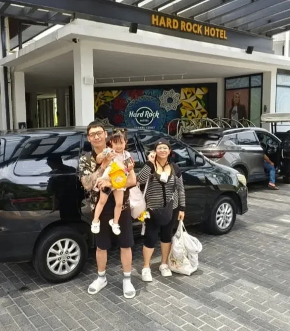 A family posing outside the Hard Rock Hotel Desaru Coast beside a black MPV