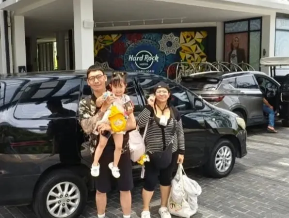 A family posing outside the Hard Rock Hotel Desaru Coast beside a black MPV