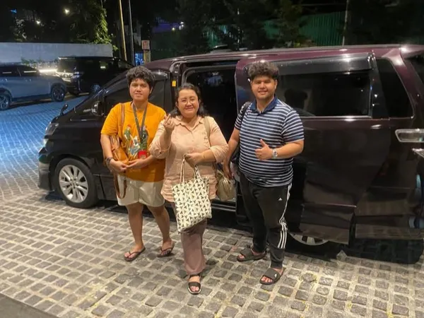 A group posing beside a maroon Toyota Alphard at night