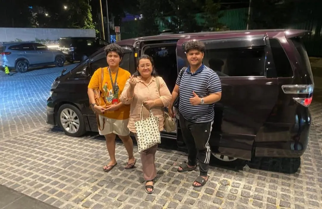 A group posing beside a maroon Toyota Alphard at night