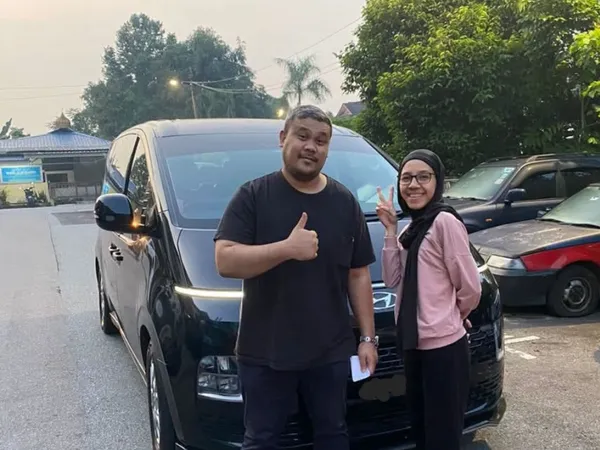 A couple posing beside a black MPV on a quiet road at dusk