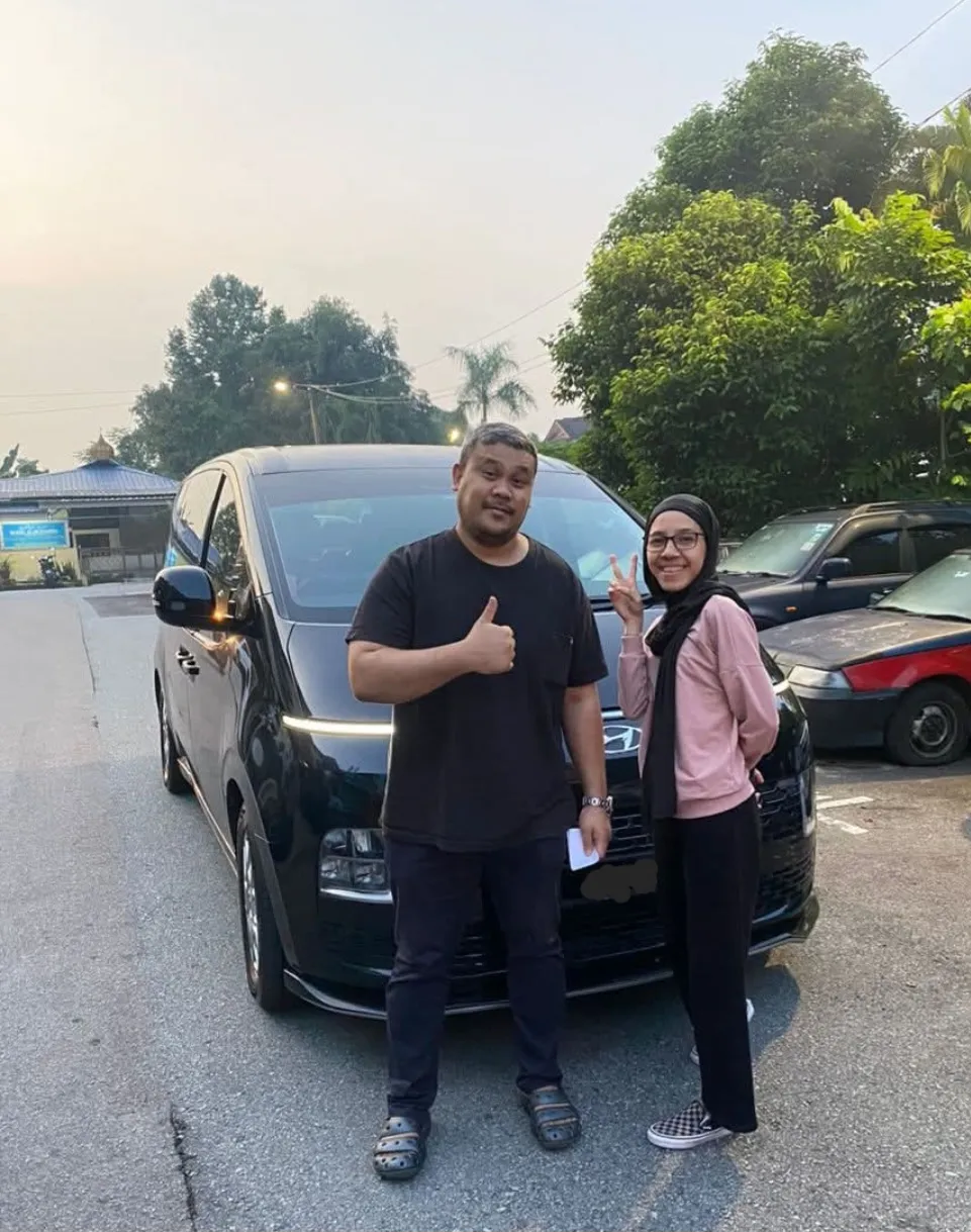 A couple posing beside a black MPV on a quiet road at dusk