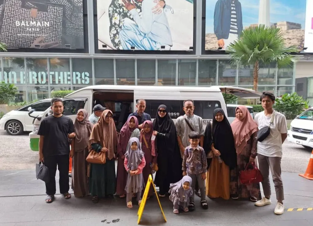 A large family group posing beside a white van outside a shopping mall