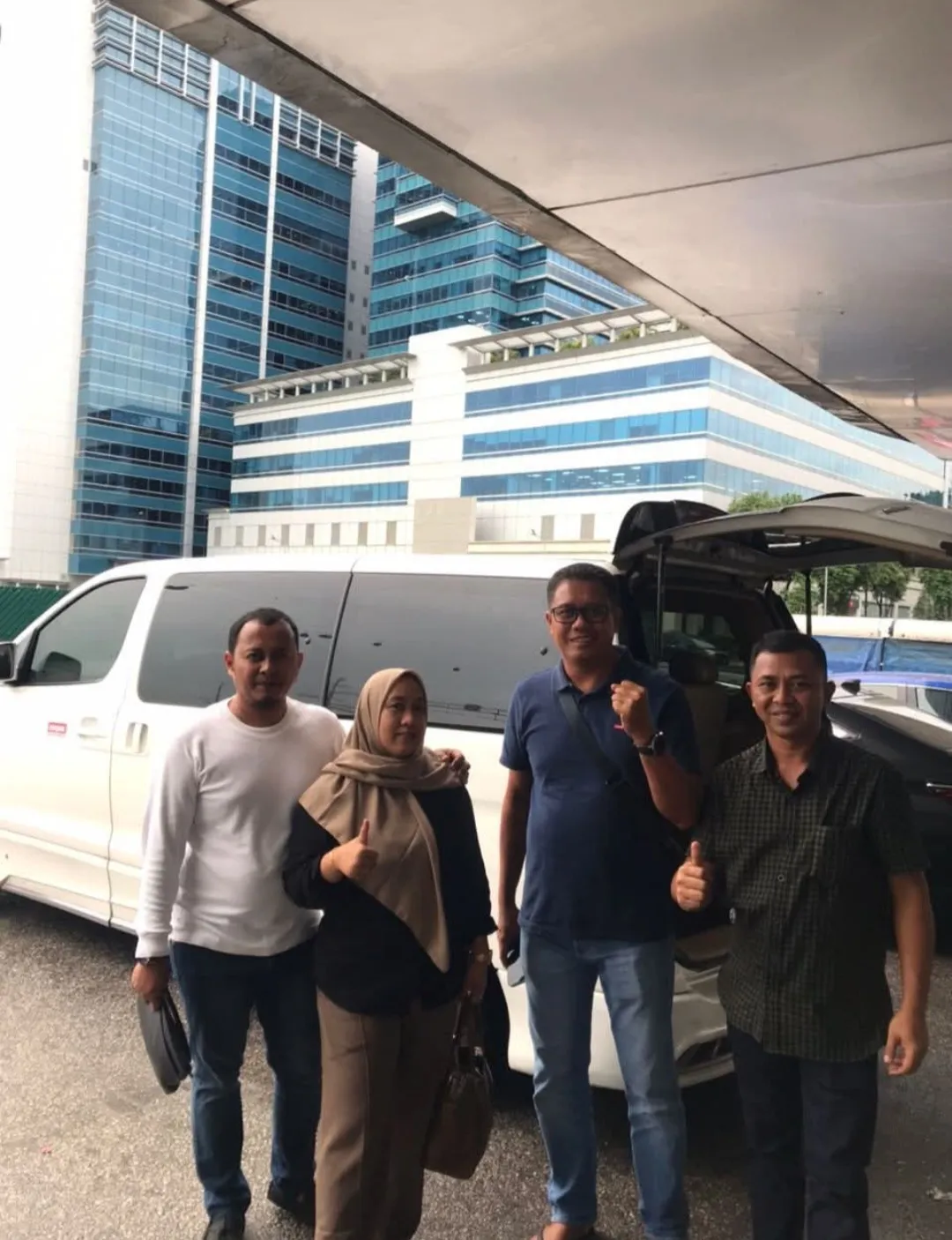 A group posing beside a white MPV with Singapore high-rise buildings in the background