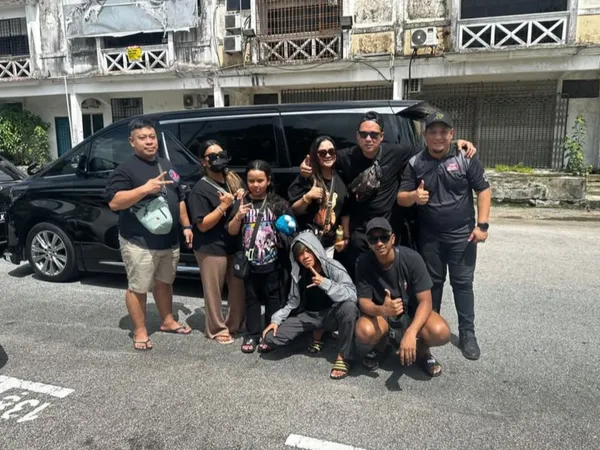 A group posing beside a black Toyota Alphard on a city street with heritage shophouses