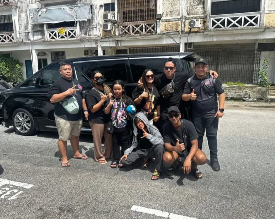 A group posing beside a black Toyota Alphard on a city street with heritage shophouses