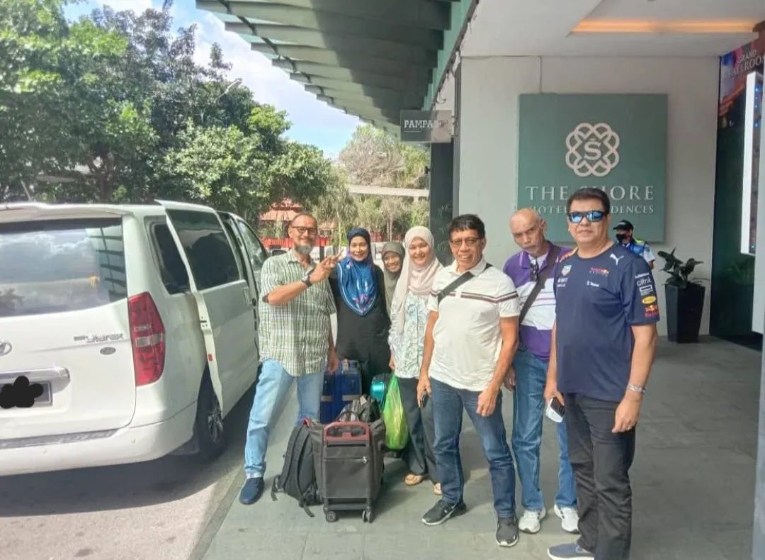 A group posing with their white Hyundai Starex chauffeur van outside The Shore Hotel Residences