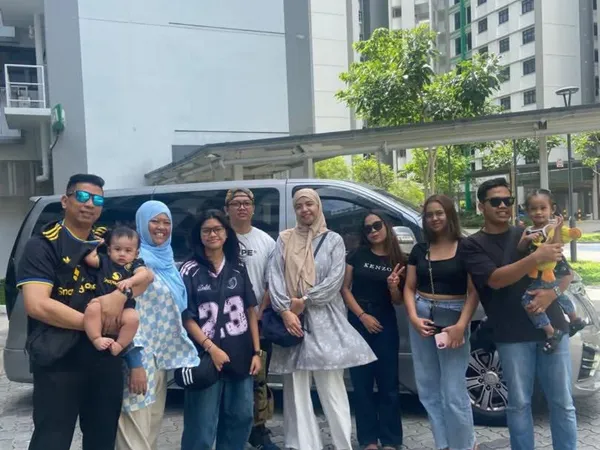 A large family group posing beside a silver MPV with Singapore housing blocks in the background