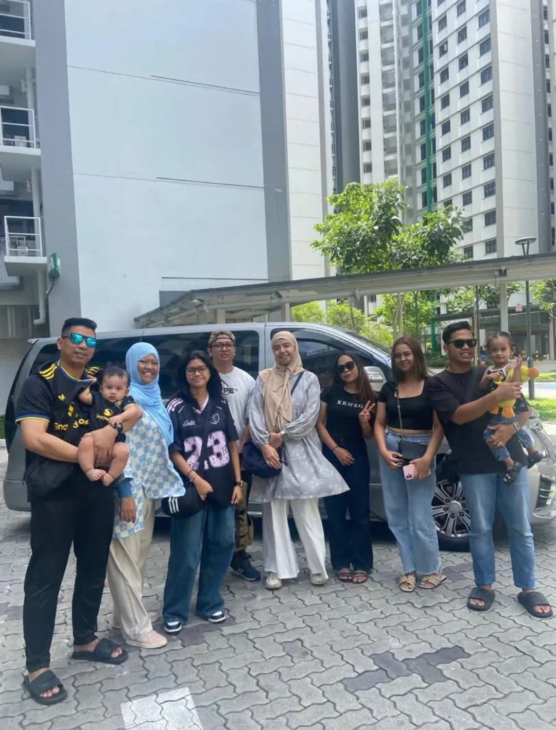 A large family group posing beside a silver MPV with Singapore housing blocks in the background