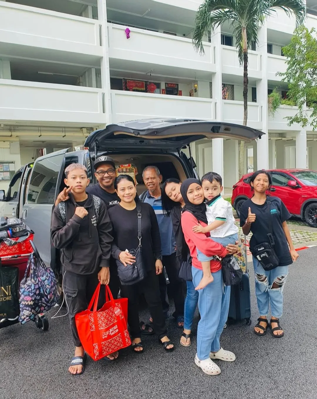 A family group posing beside a black van with Singapore housing blocks in the background