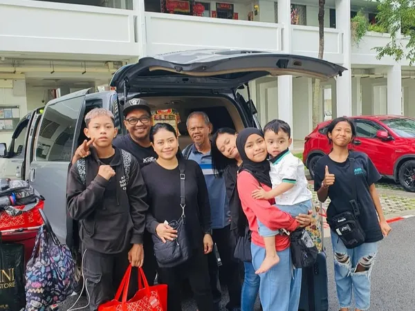 A family group posing beside a black van with Singapore housing blocks in the background