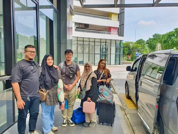A family posing outside a modern building beside a silver MPV
