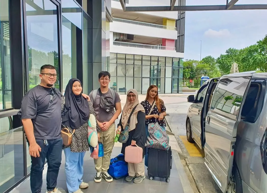 A family posing outside a modern building beside a silver MPV