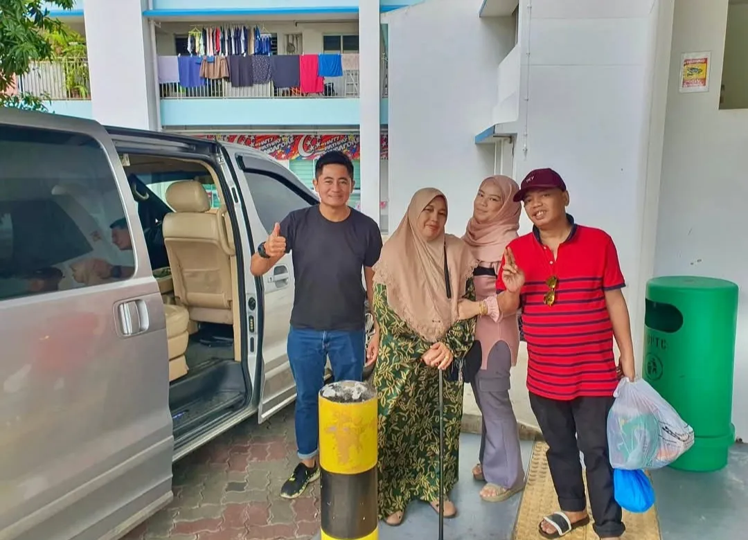 A group posing beside a silver MPV outside a Singapore housing block