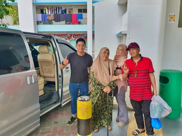 A group posing beside a silver MPV outside a Singapore housing block