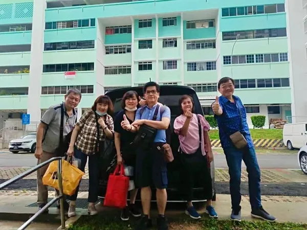 A group posing beside a black MPV outside a Singapore housing block