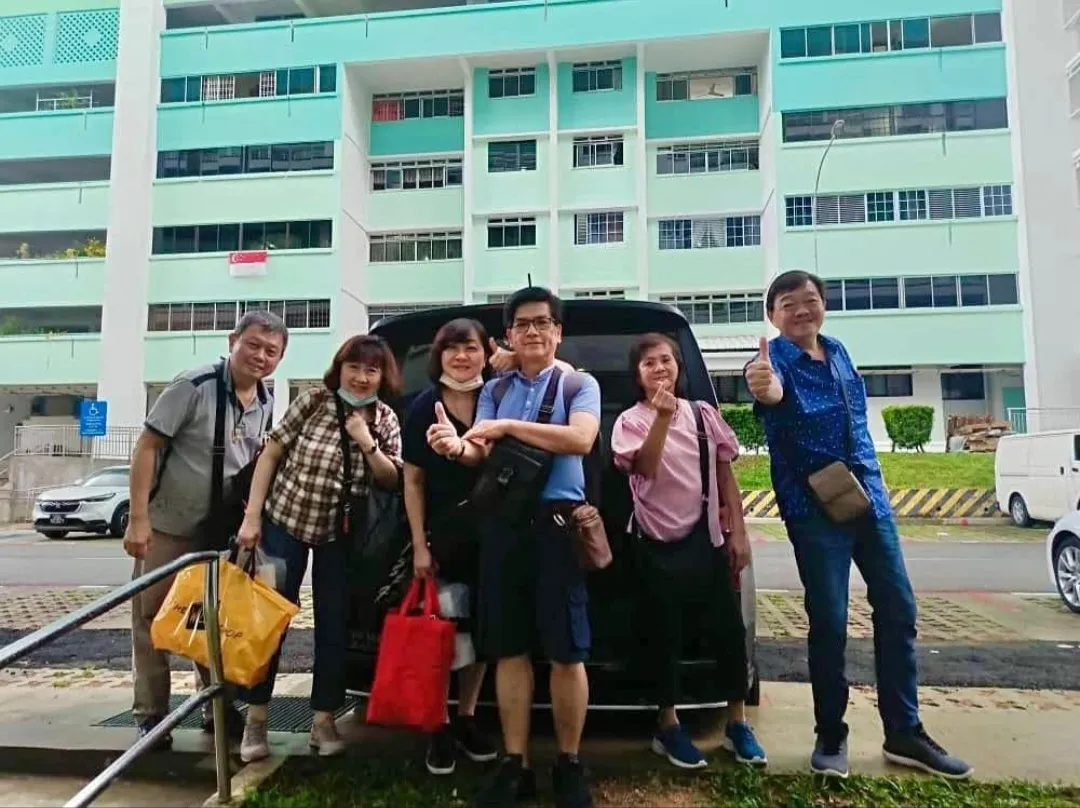 A group posing beside a black MPV outside a Singapore housing block