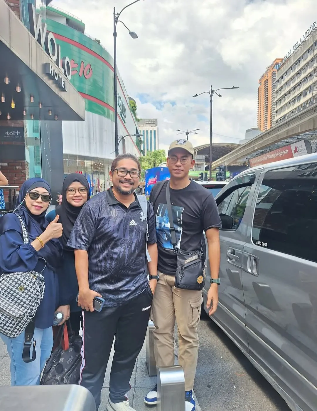 A group posing beside a silver van outside the WOLO Hotel in Kuala Lumpur