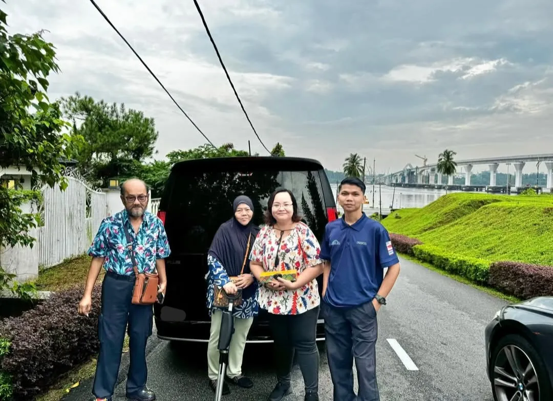 A family posing with their chauffeur van beside a river, with a bridge in the background