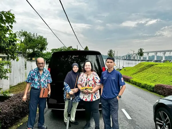 A family posing with their chauffeur van beside a river, with a bridge in the background