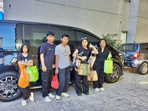 A family with shopping bags posing beside a black MPV in the evening