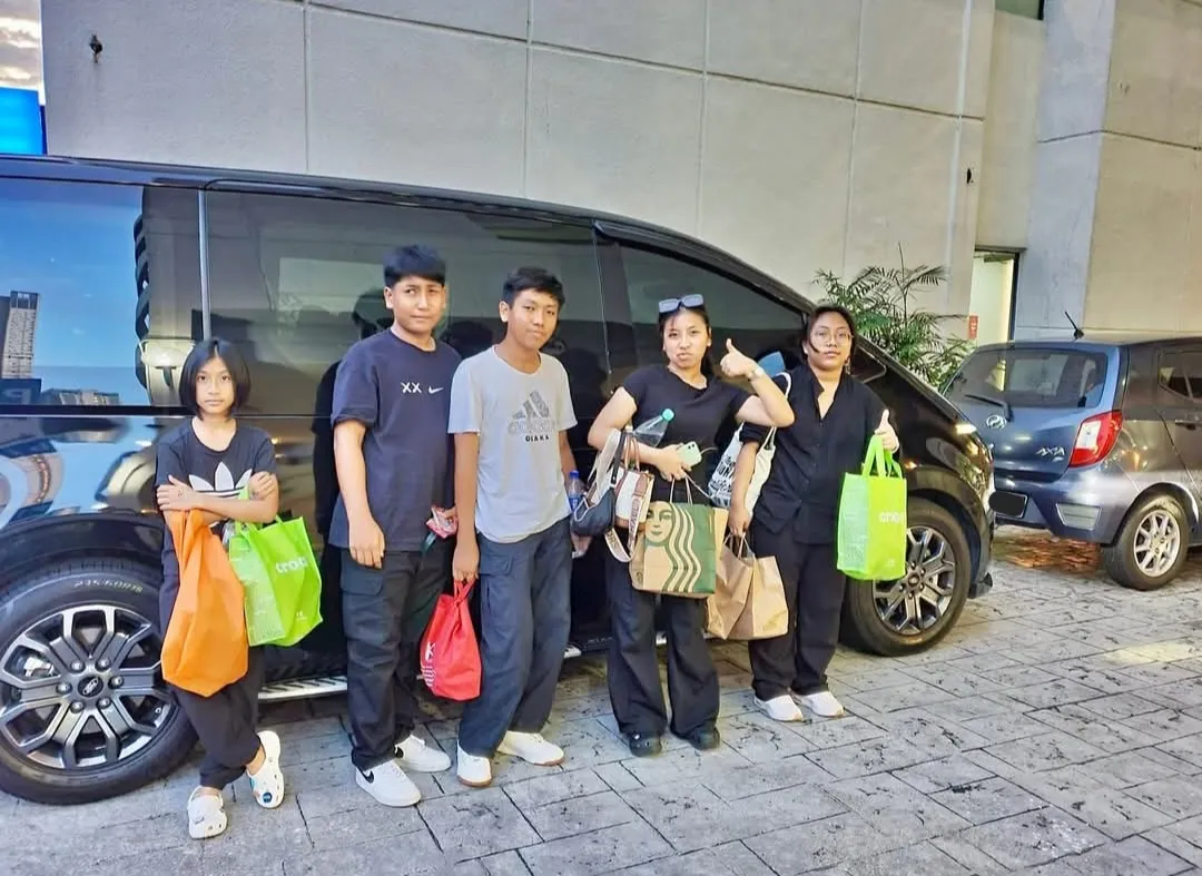 A family with shopping bags posing beside a black MPV in the evening