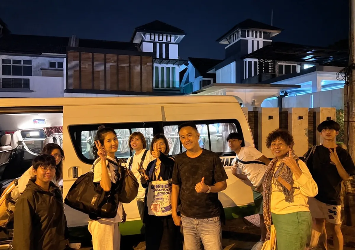 A large group posing beside a white van at night near resort-style buildings