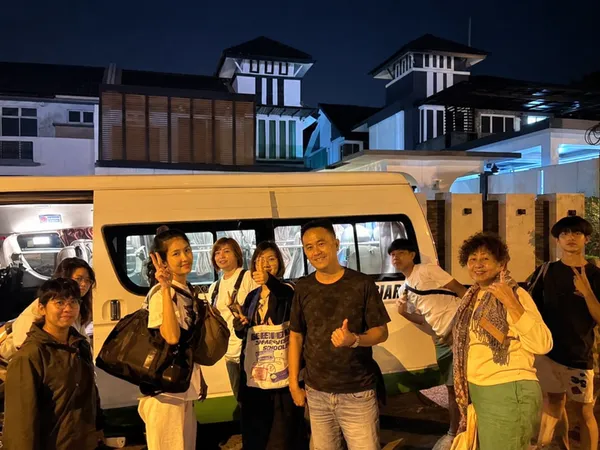 A large group posing beside a white van at night near resort-style buildings