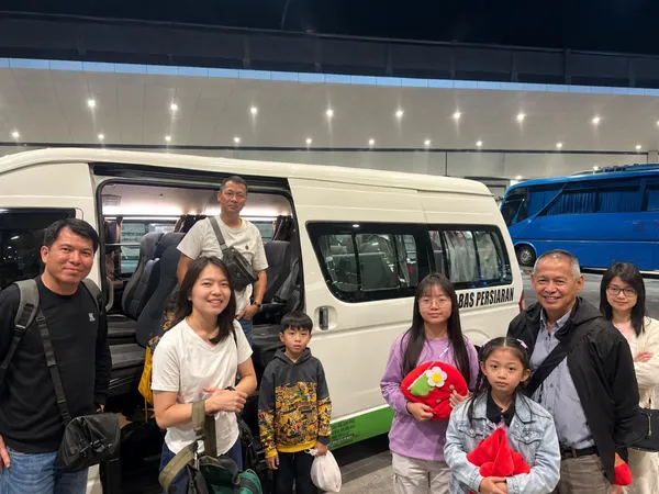 A family holding flower toys beside a Bas Persiaran tour bus at night