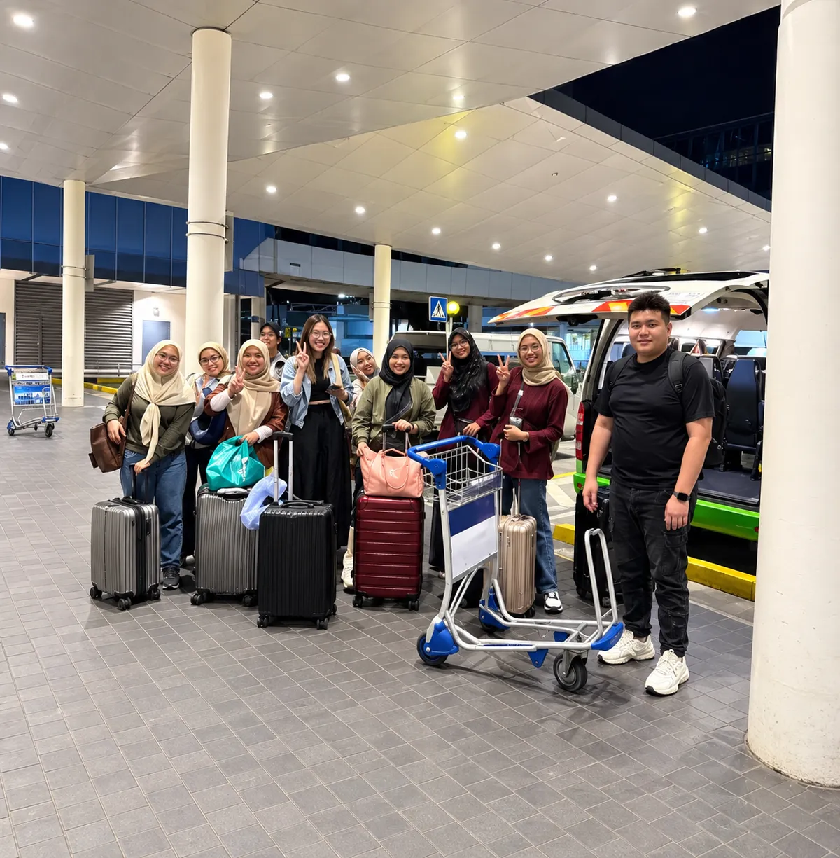A group with a luggage cart at an airport terminal at night
