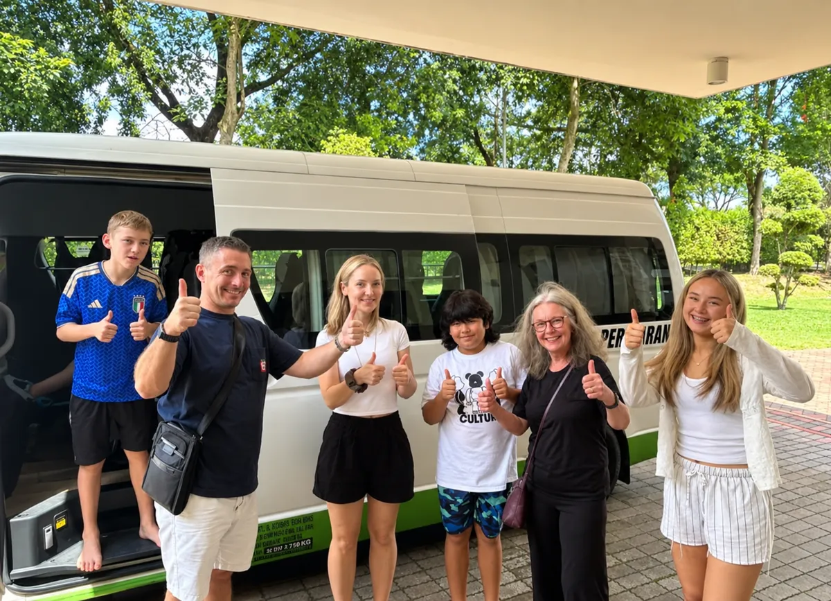 An international family giving thumbs up beside a Persiaran tour bus in a park setting