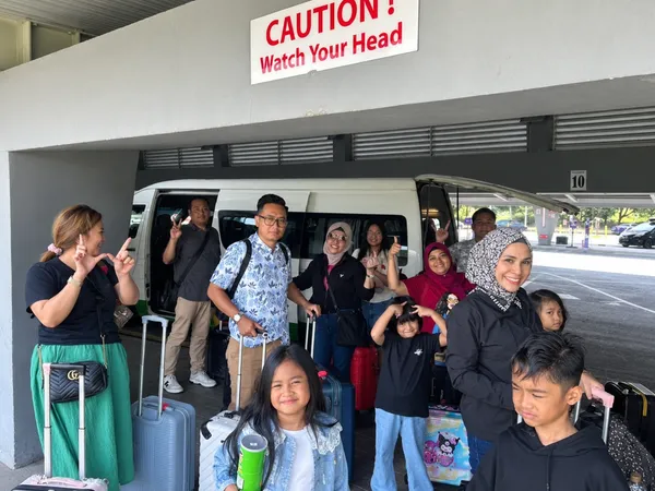 A large family group with luggage beside a tour van at an airport terminal