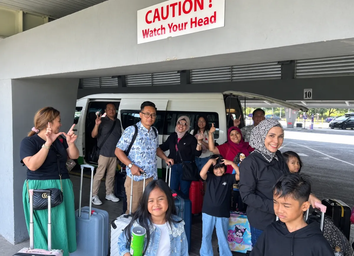 A large family group with luggage beside a tour van at an airport terminal